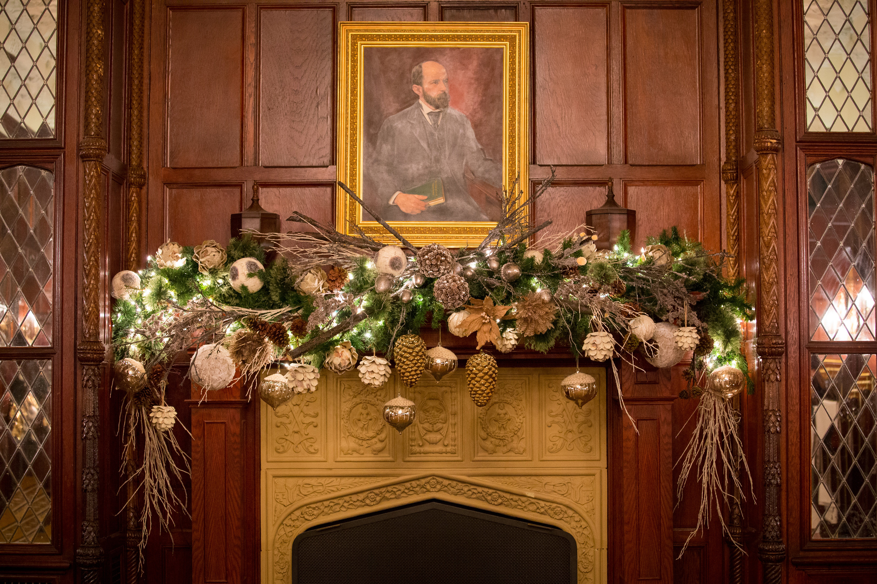 A decorated fireplace mantel with a portrait above it in a lobby or public area.