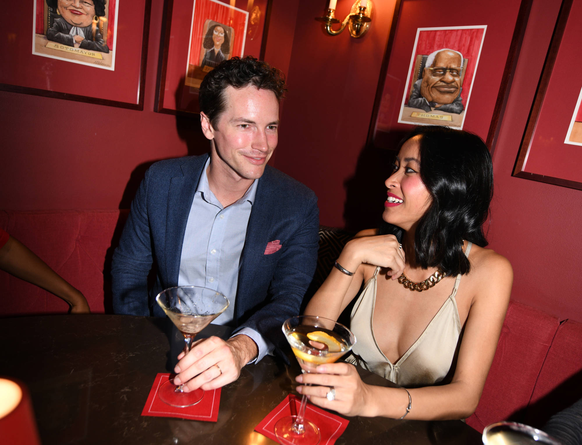 A man and woman sit at a table in a bar, each holding a martini glass.