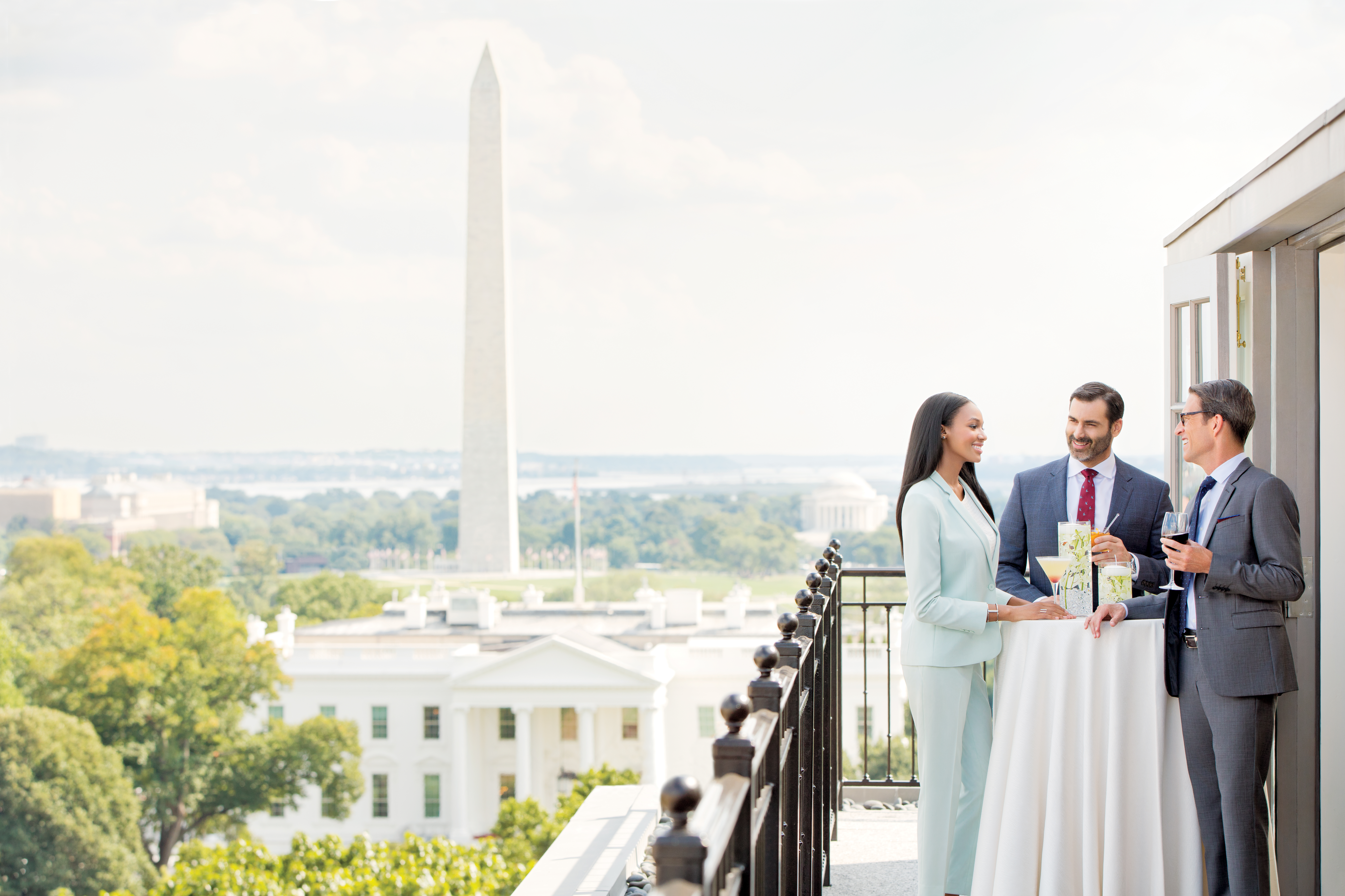 Three formally dressed people standing on a balcony with a view of the White House and Washington Monument