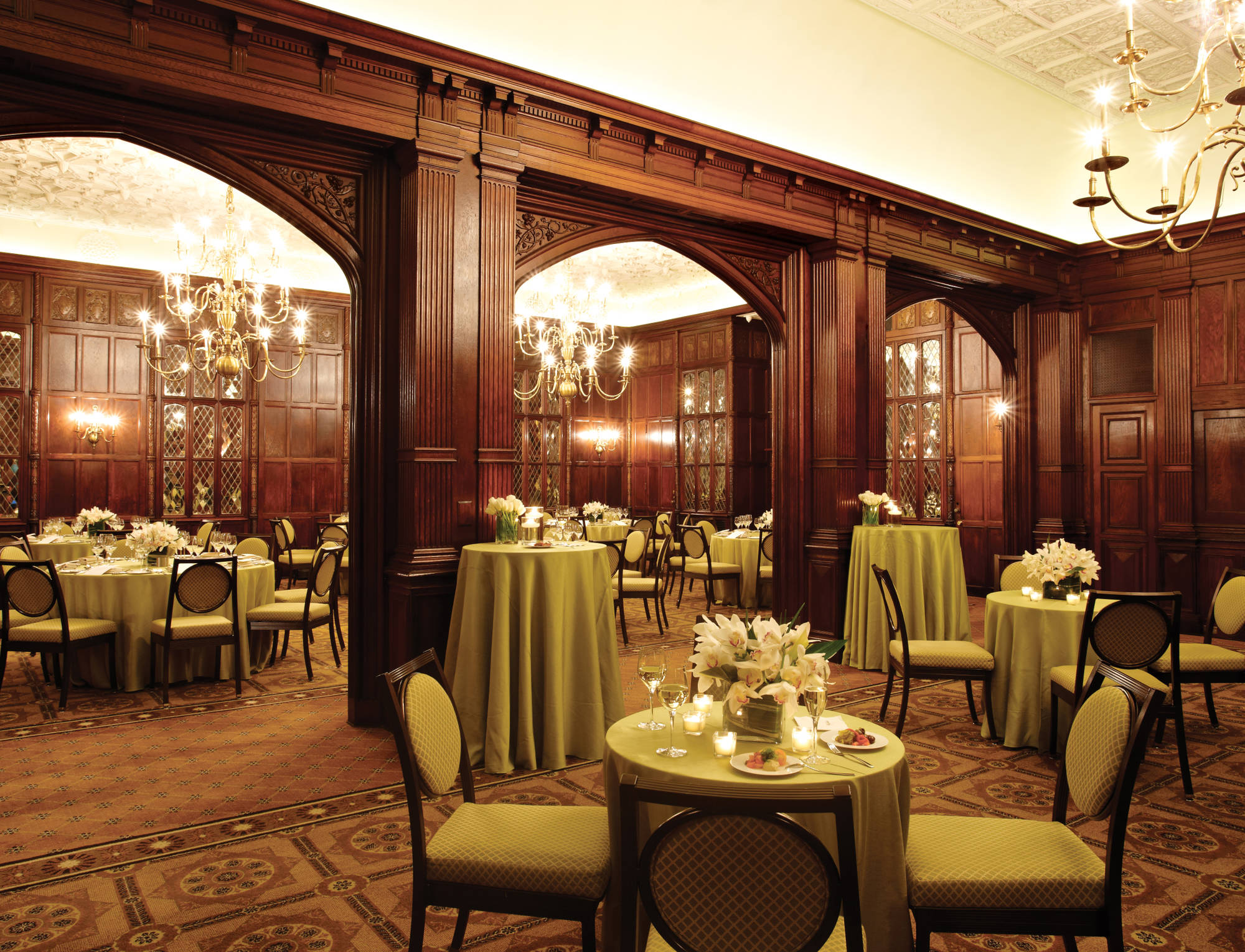 A luxurious lounge with round tables, chairs, chandeliers, and floral arrangements.