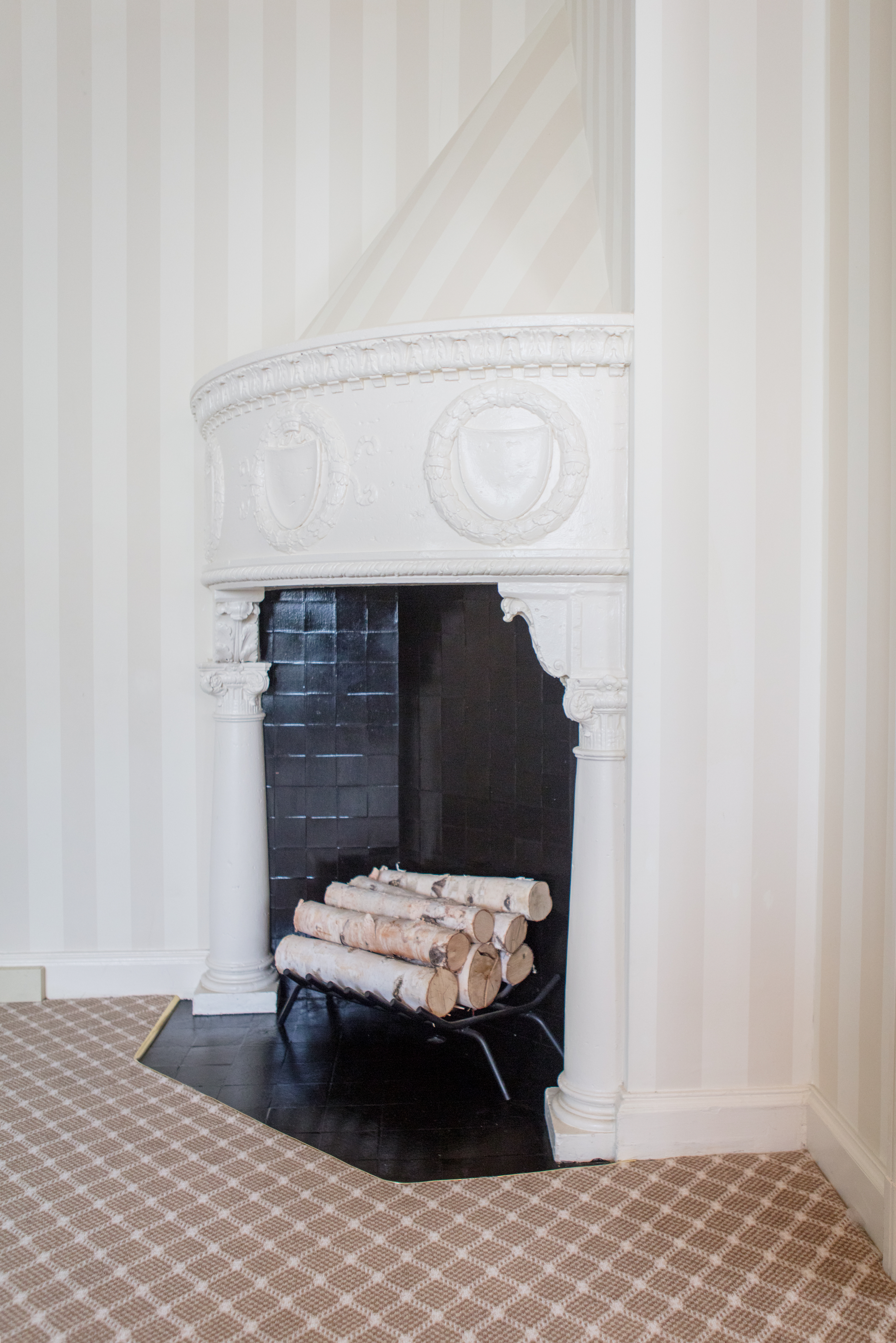A white fireplace with a black interior and wood logs inside.