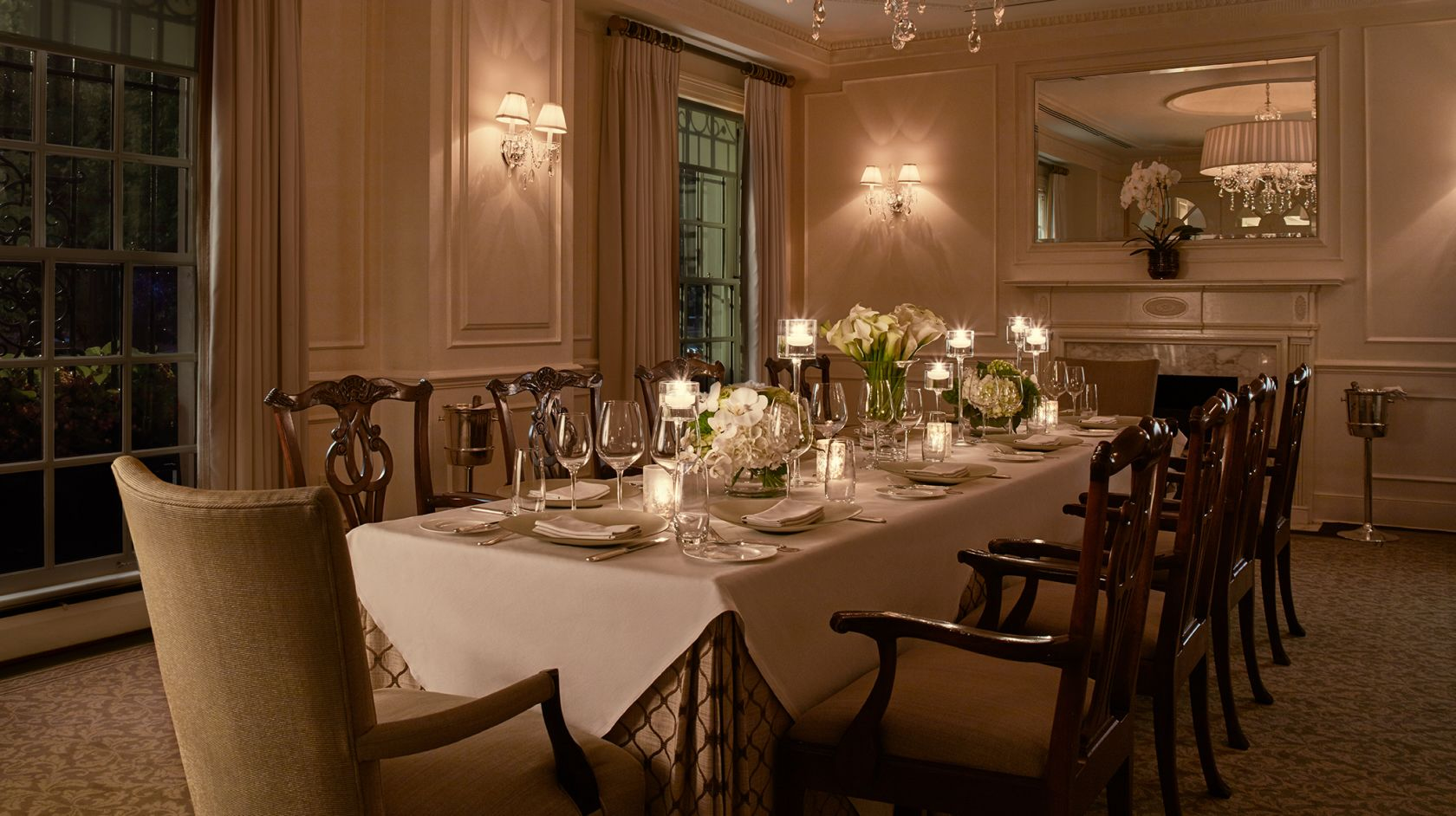 A formal dining room with a long table set for dinner, adorned with white flowers, candles, and wine glasses.