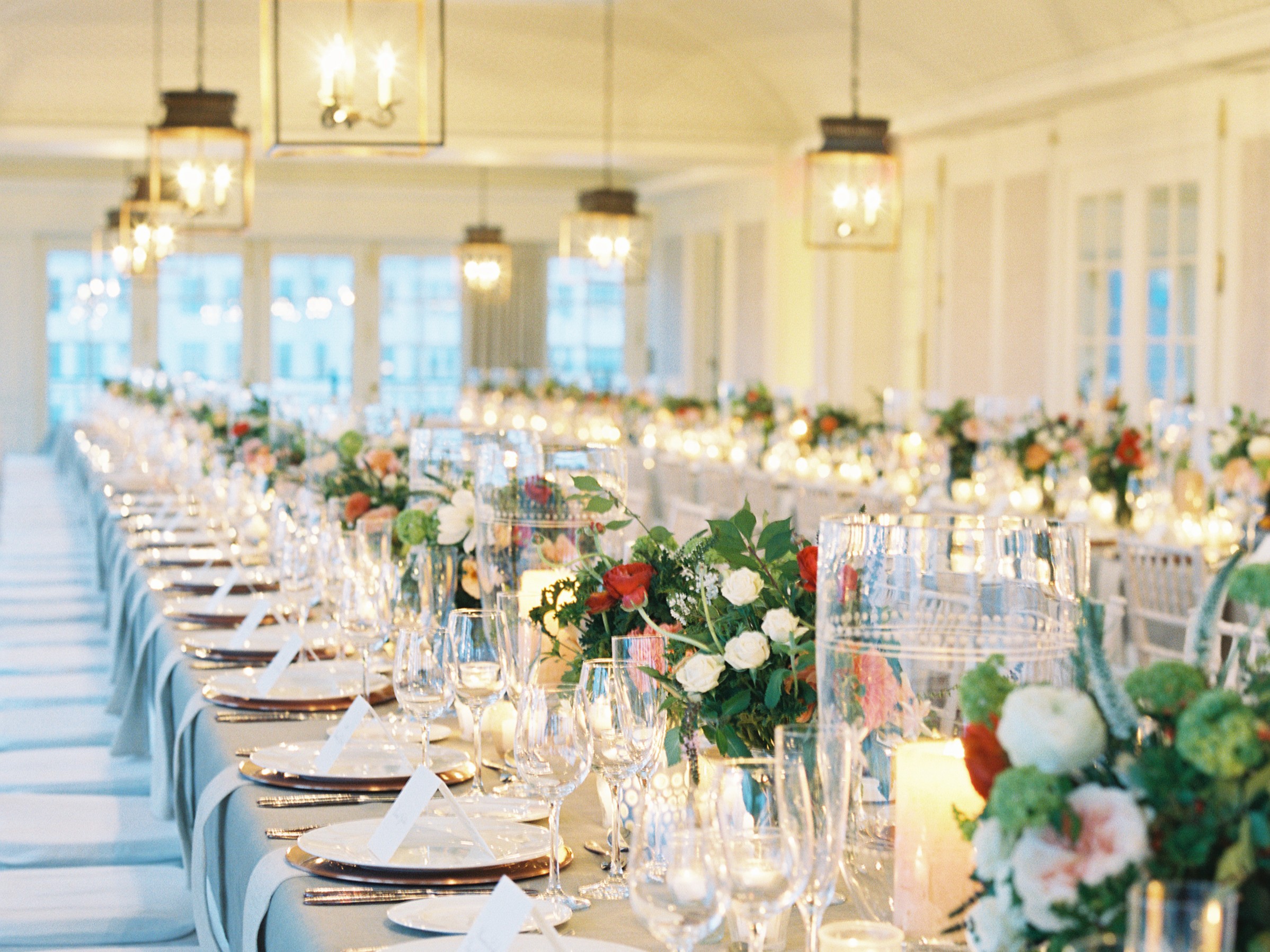 A long, elegantly set dining table in a bright, white room with flowers and candles as centerpieces.