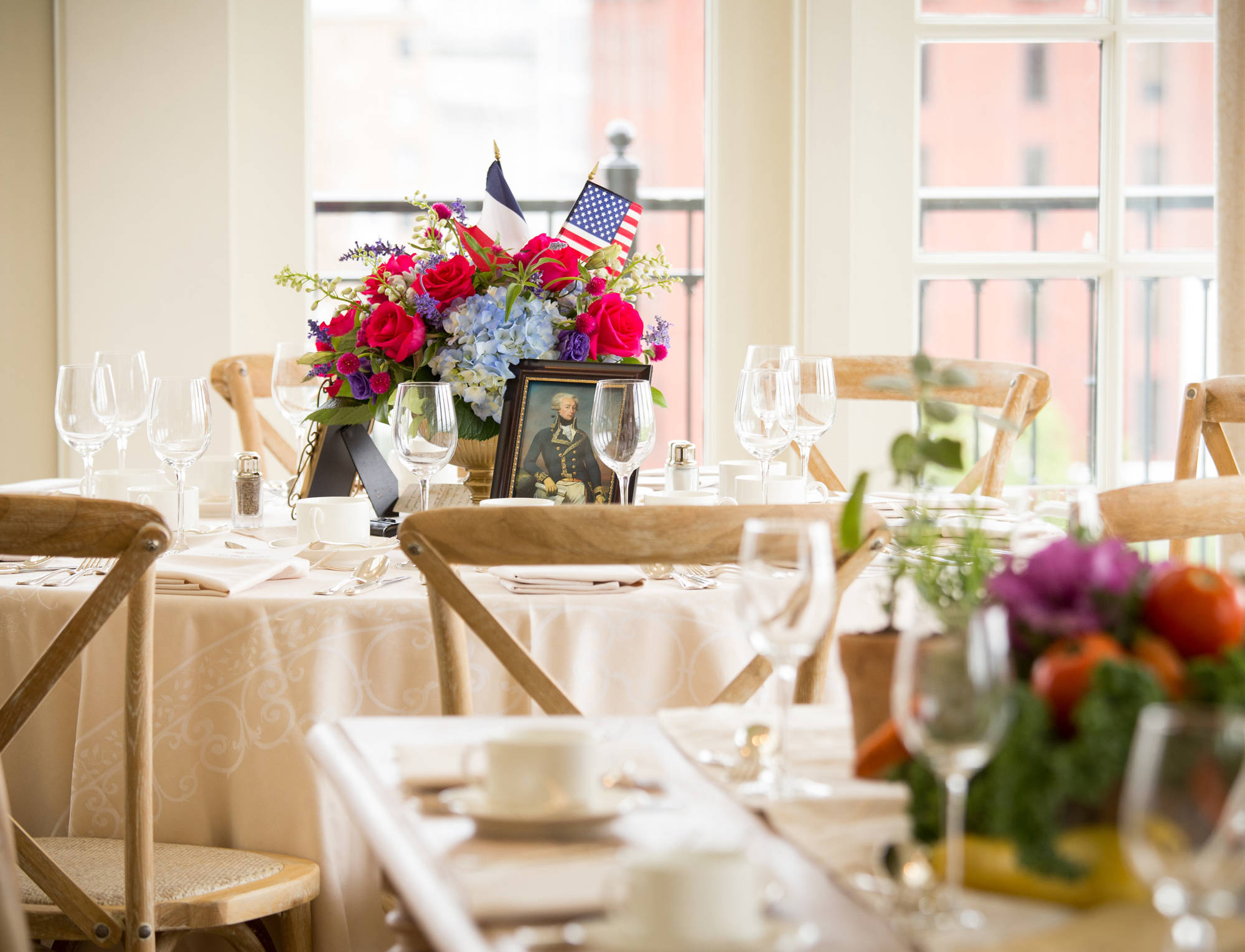 A dining table set with flowers, wine glasses, and a portrait of a man in a military uniform.